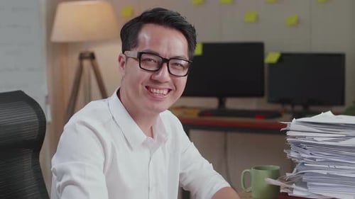 Close Up Of Asian Man Smiling To Camera While Working With Documents At The Office