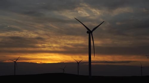 Bewegen Sie die Blätter einer großen Windkraftanlage in einem Feld vor dem Hintergrund des orangefarbenen Sonnenuntergangs auf dem