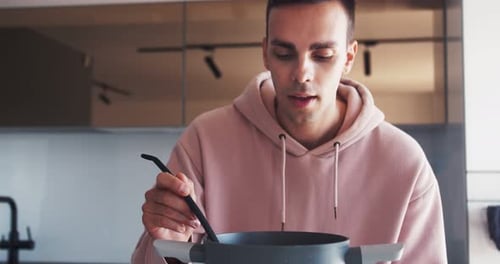 Man in Pink Hoodie Tastes Soup with Ladle