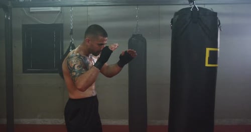 Shirtless Man Kicking Boxing Bag in Gym
