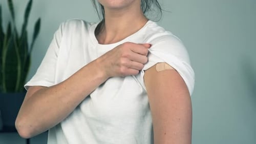 Woman Points to Bandage on Her Arm