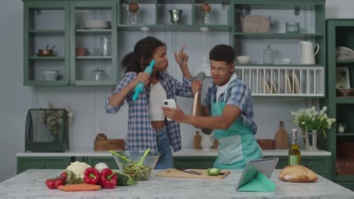 Enthusiastic Young Couple Singing and Dancing in Kitchen