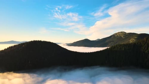 Aerial view of a big mountain over white dense clouds at bright sunrise.