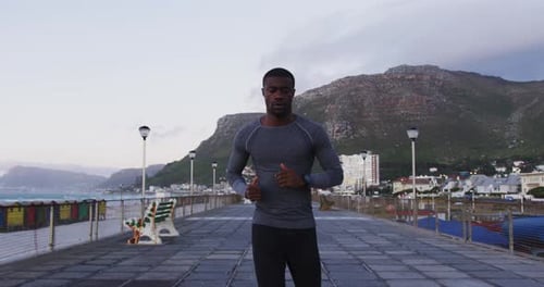 Focused african american man exercising outdoors, running by seaside