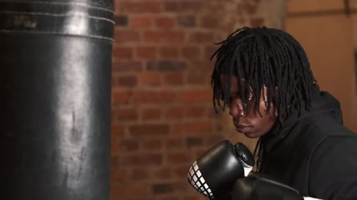 Dedicated Young Man Punching Boxing Bag at Gym
