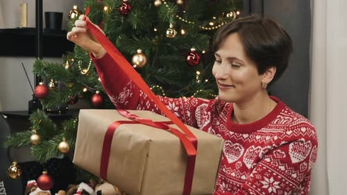 Woman Opens Gift by Christmas Tree