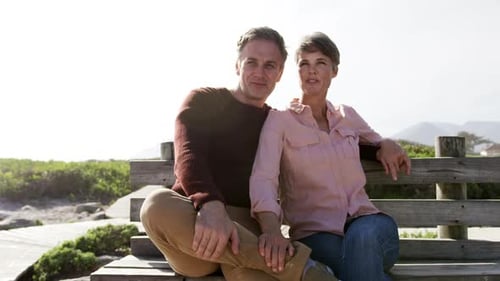 Caucasian couple enjoying free time by sea on sunny day sitting on bench