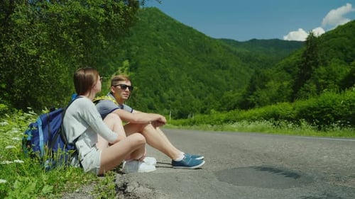 Young Couple Relaxing on Roadside Near Green Hills