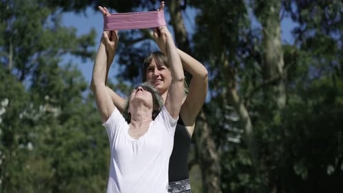 Woman Assists Senior with Resistance Band Stretch Outdoors