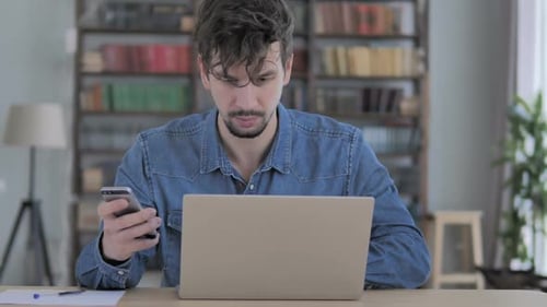 Young Adult Using Laptop and Smartphone at Desk