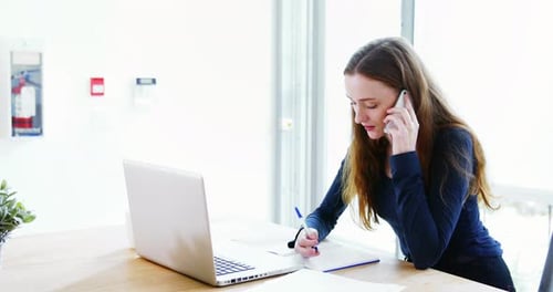 Young Woman Talking on Phone, Working on Laptop