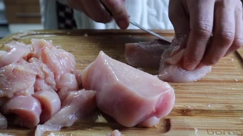 Hände schneiden frisches Hähnchenfleischfilet auf Holzschneidebrett in der Küche - Nahaufnahme