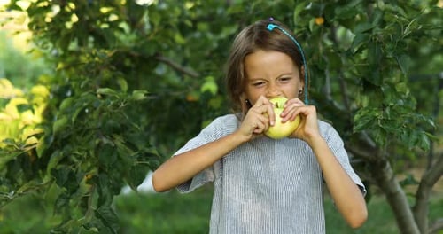 Nettes kleines Mädchen isst grünen Apfel im Hausgarten im Freien, glückliches Kind