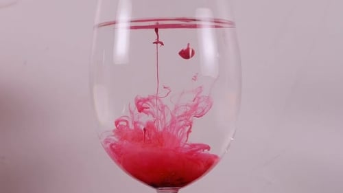 Red Ink Swirls in a Wine Glass Against a White Background