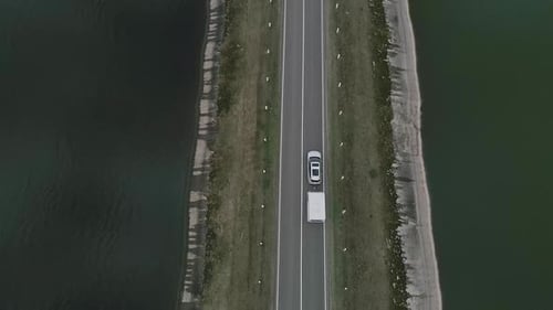 A Car with a Camper Rides on Road Across a River in Iceland. Family Trip. Aerial