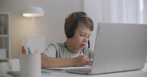 School Boy Is Drawing at Home and Talking By Internet with Friend, Using Laptop and Headphones with