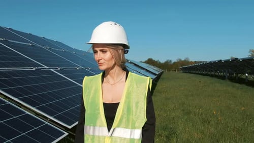 Industrieingenieurin in Uniform geht zur Prüfung durch das Feld eines Solarmoduls