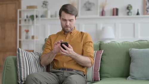Man Sitting on Couch Using Smartphone