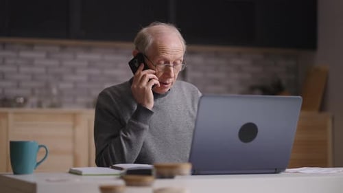 Senior Man Talking on Smartphone, Working on Laptop