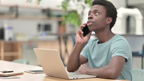Young Adult Using Phone at Desk With Laptop