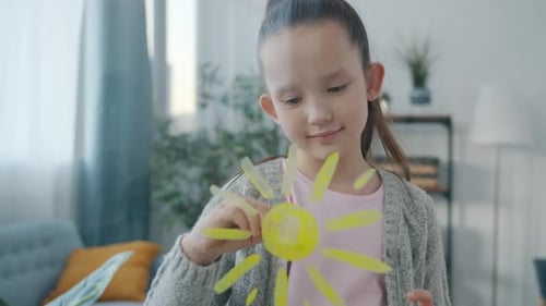 Porträt eines kleinen Mädchens, das Sonne auf Glas malt und allein zu Hause lächelt