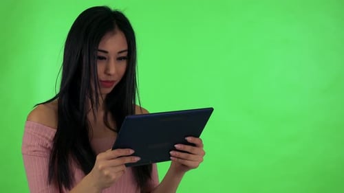 Young Attractive Asian Woman Works on Tablet and Smiles - Green Screen Studio