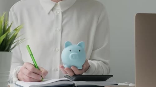 Empresaria escribiendo en el libro de cuentas bancarias y poniendo monedas en una alcancía