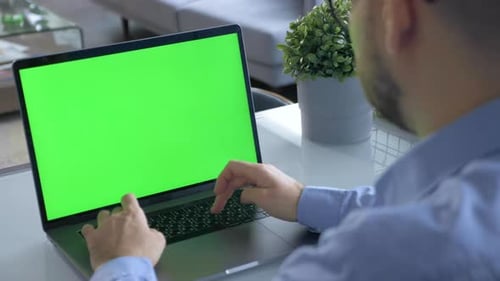 A man using a laptop with a green screen in the office at home