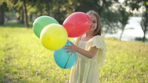 Positive Girl Playing with Multicolored Balloons on Sunny Day in Spring Summer Park