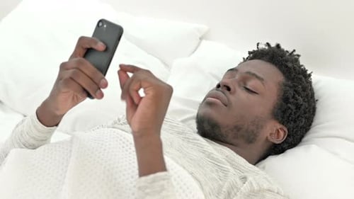 Young Adult Uses Phone While Lying in Bed
