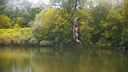 Young Man Flying Above the Water Holding By the Bar