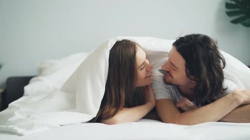 Fille et mec parlant baisers s'amusant au lit ensemble en profitant d'une relation