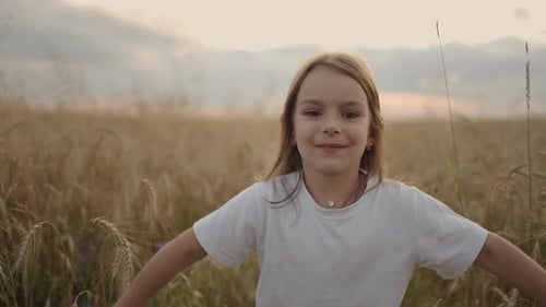 Slow Motion a Little Girl of 45 Years Old Runs in a Field at Sunset Looking at the Camera Happy and