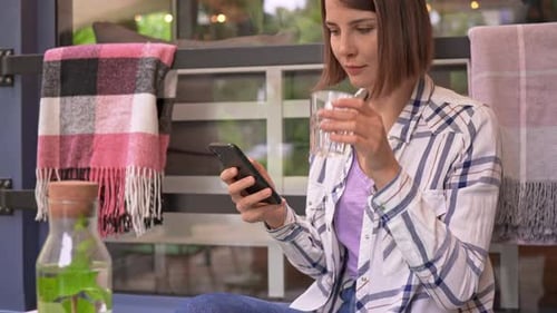 Woman Using Smartphone in Cafe, Drinking Water