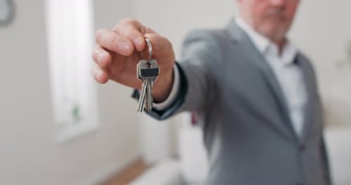 Shot of Apartment Keys Extended on Palm of Hand Toward Camera Grayhaired Mature Man Dressed in Suit