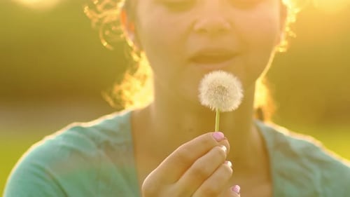 Woman Blowing Dandelion Seeds in Golden Light