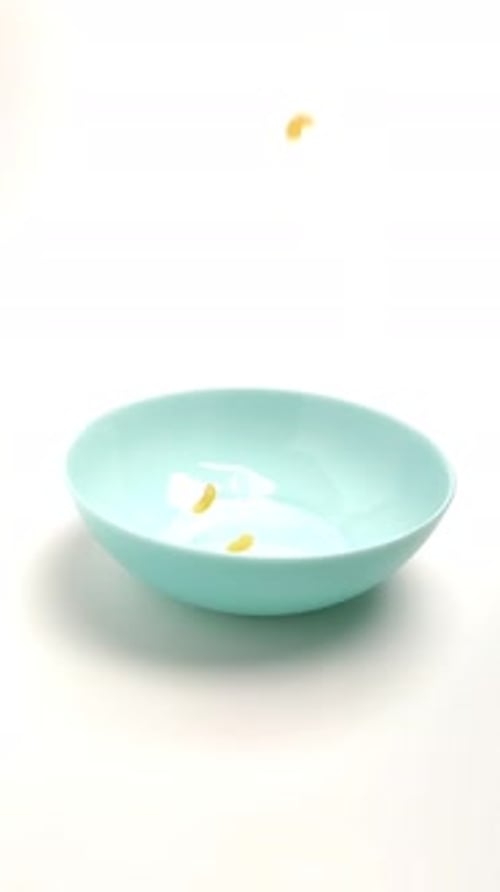 Wheat Pasta Falls on a Blue Plate on a White Background. Close-up, Slow-motion