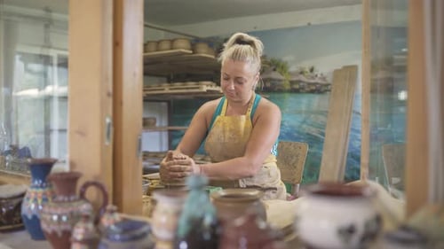 Vue de face d'une potière blonde faisant de la poterie sur une roue de potier