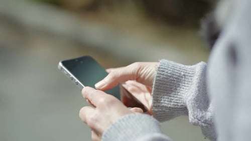 Female Hands Typing Message on Smartphone Outdoor.