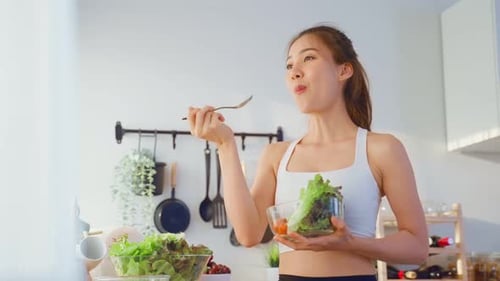 Young Adult Woman Eats Salad in Kitchen