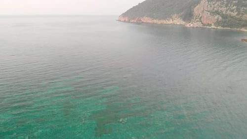 Aerial drone footage of calm sea with mountain in the background.