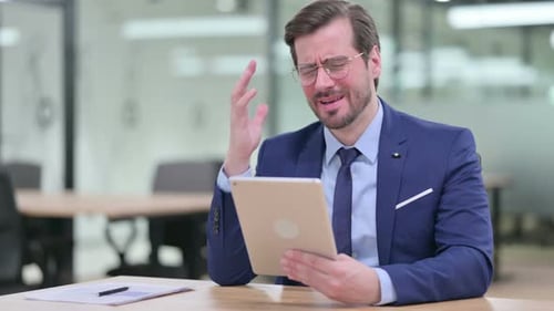Businessman Using Tablet Expresses Frustration at Office Desk
