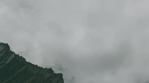 Timelapse Clouds Swirl Over a Mountain Valley a Snowy Peak in the Distance