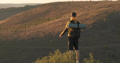 Jovem viajante com câmera parado no topo da rocha e olhando para o pôr do sol, turista masculino com