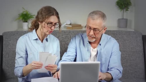 Mature Couple Reviews Bills with Laptop At Home