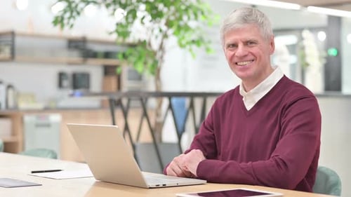 Smiling Mature Man Working on Laptop in Modern Office