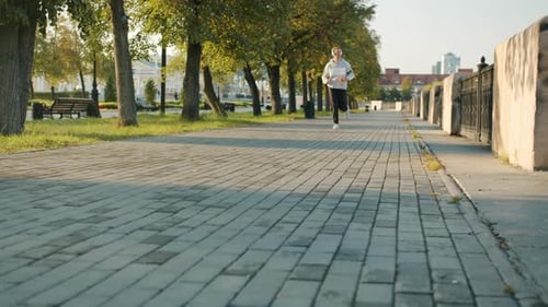 Low Shot of Fit Young Man Wearing Headphones Jogging Outdoors in City Street