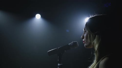 Close-up of the Face of the Singer with Microphone on a Black Smoky Background. The Singer Sings a