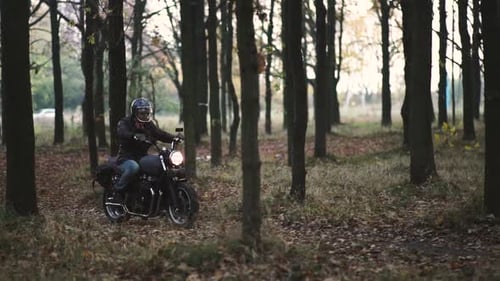 Man Riding Old Custom Caferacer Motorcycle on Forest Country Road at Sunset