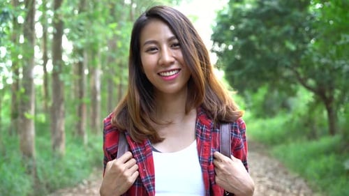 Happy young Asian woman traveler with backpack walking in forest.